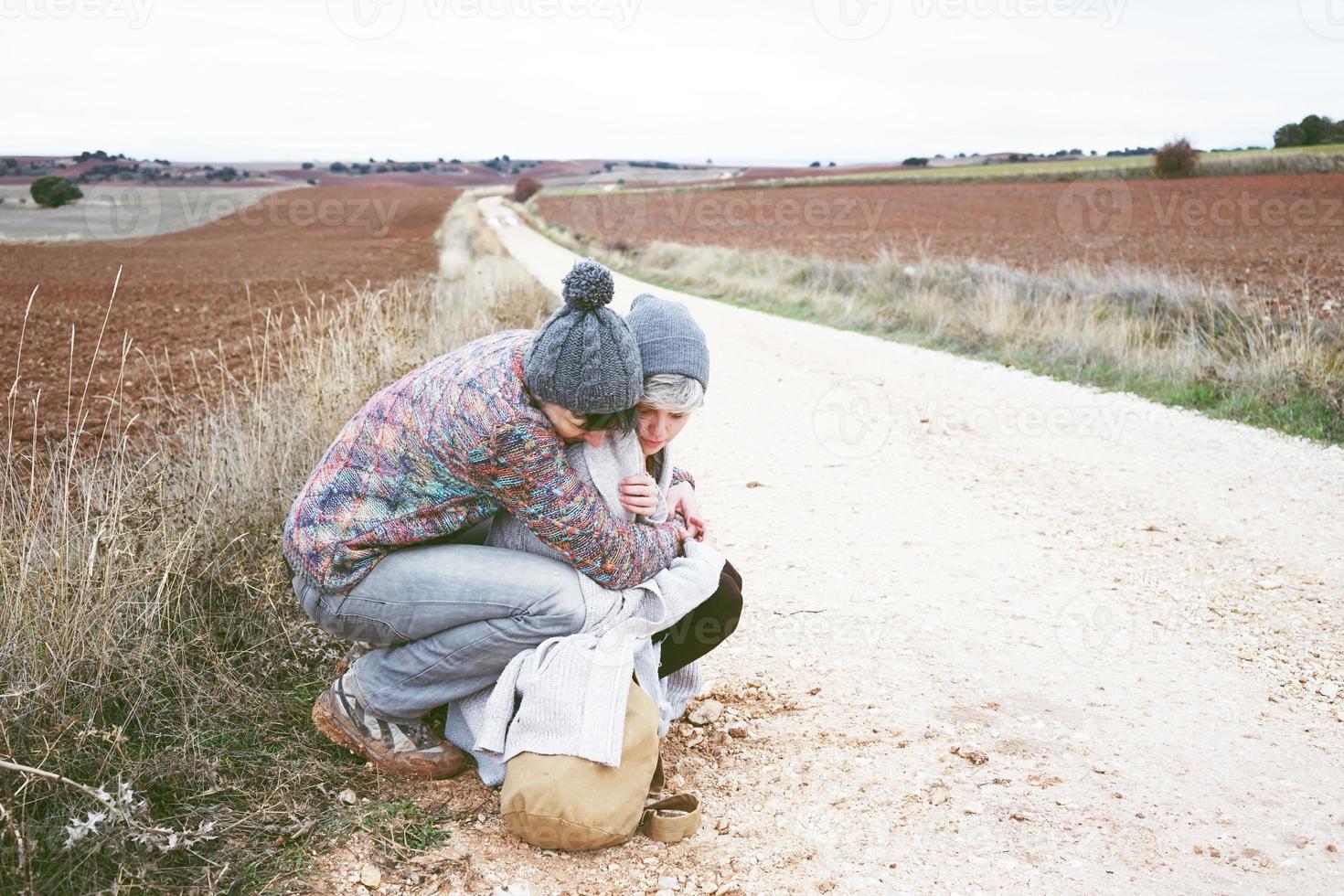 Pareja de jóvenes millennials abrazándose y descansando junto a una mochila en un viaje de aventura en un camino rural al aire libre foto