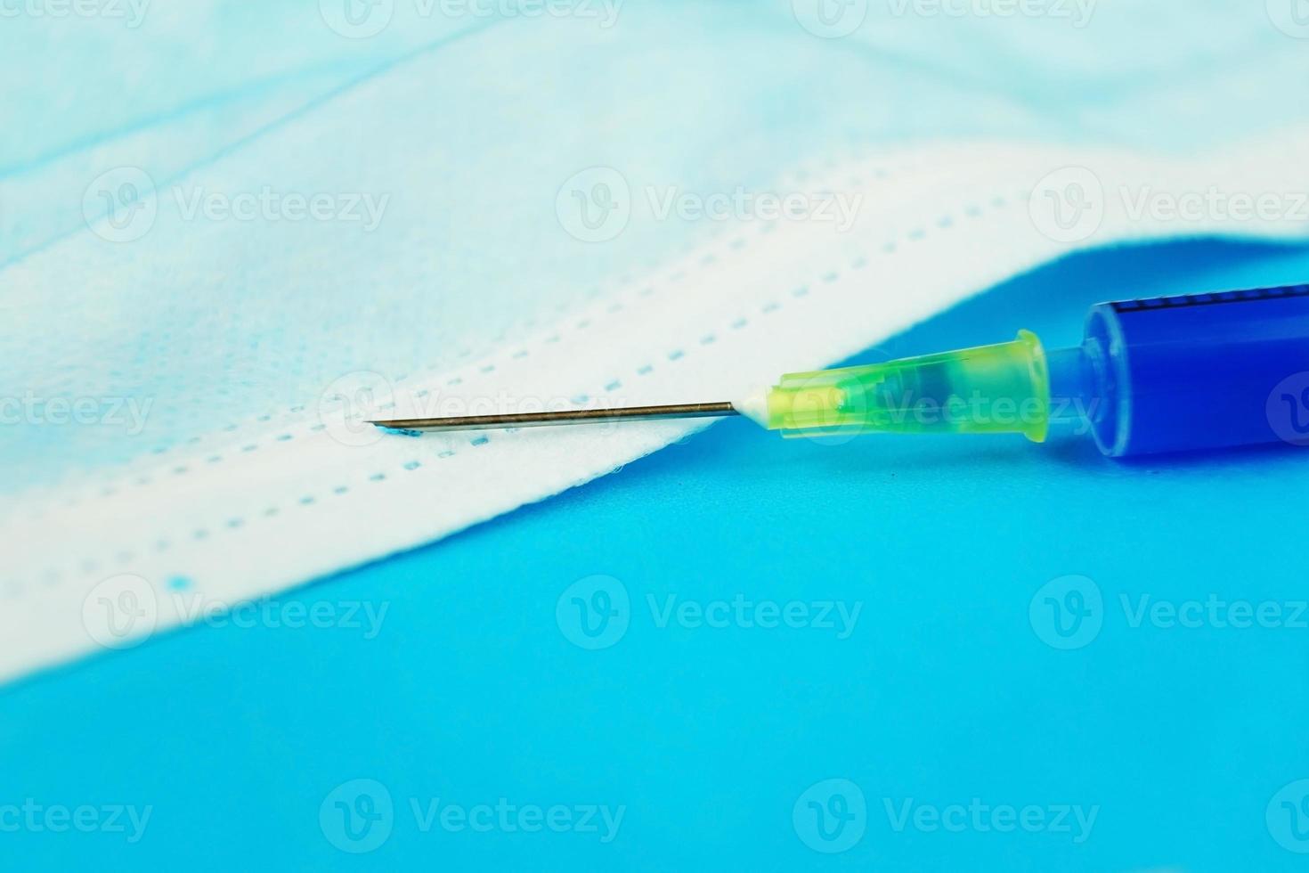 A detailed macro of a syringe with needle on a medical mask with blue background photo