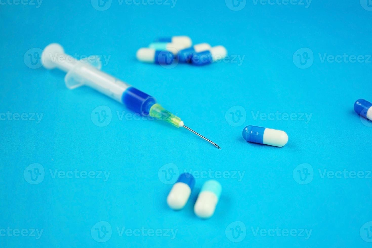 A detailed macro of a syringe by pills with needle and blue background photo