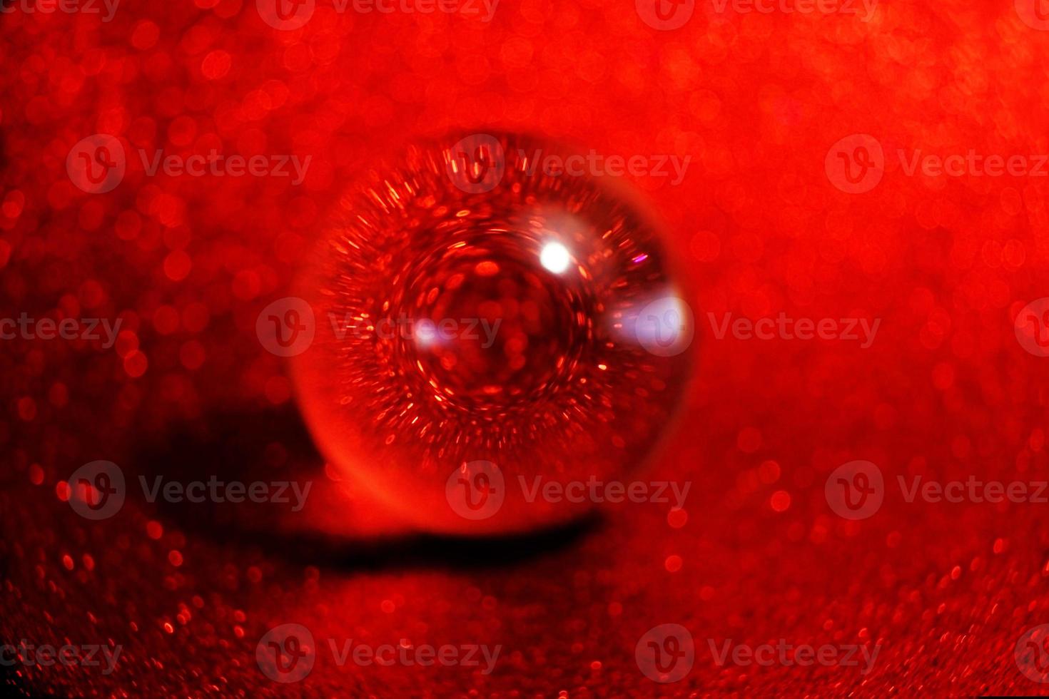 Una macro asombrosa y hermosa de una esfera de cristal sobre un fondo purpurin purpurina roja que parece una gota de agua foto