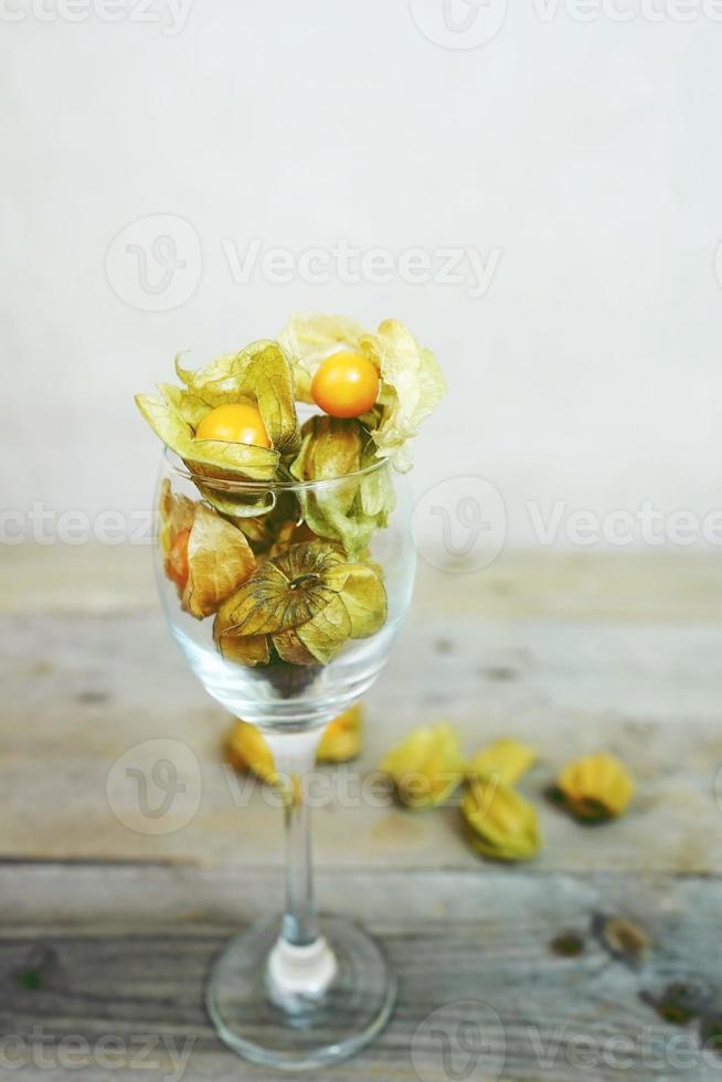 Hermoso y elegante primer plano macro de un lote de fruta sabrosa naranja llamada Physalis de Perú, América del Sur, en un vaso de cristal sobre mesas de madera foto