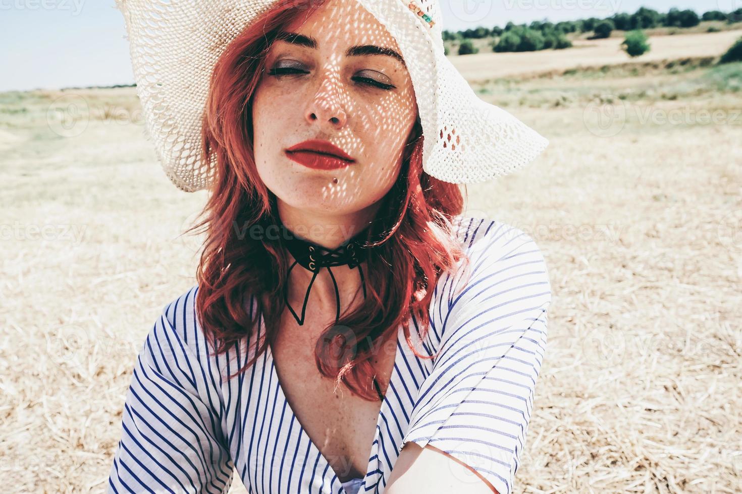 modelo pelirroja protegiéndose del sol con un sombrero en verano foto