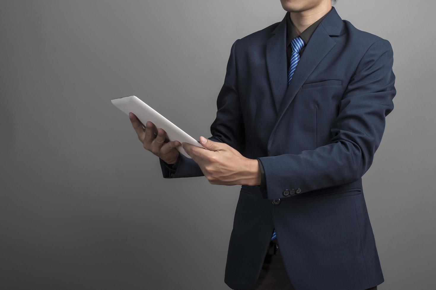 Close up of businessman in blue suit using tablet computer on gray background photo