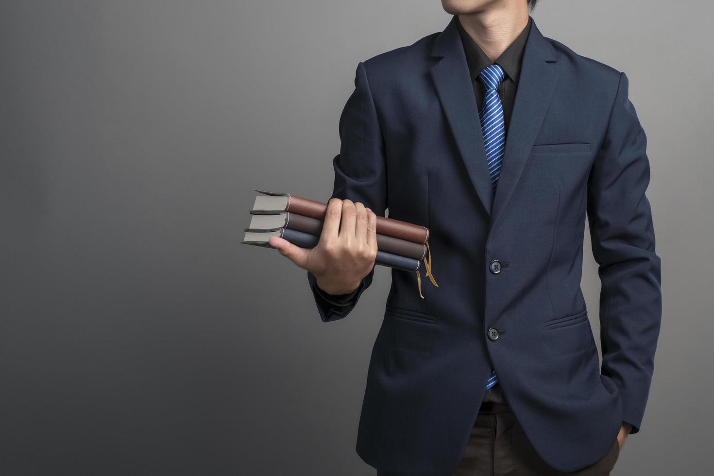 Close up of businessman in blue suit holding books on gray background photo