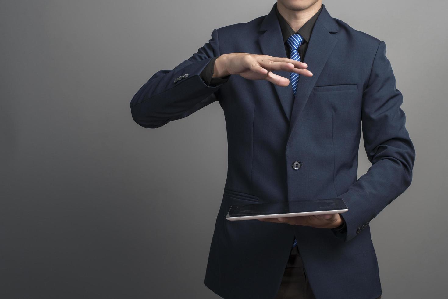 Close up of businessman in blue suit using tablet computer on gray background photo