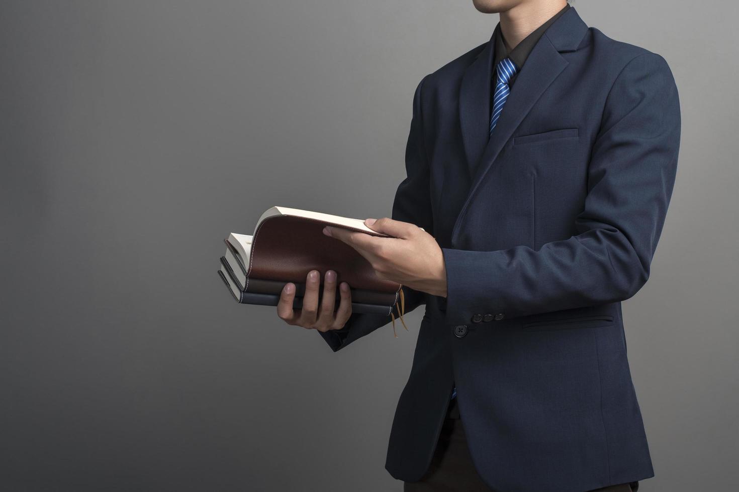 Cerca del empresario en traje azul sosteniendo libros sobre fondo gris foto