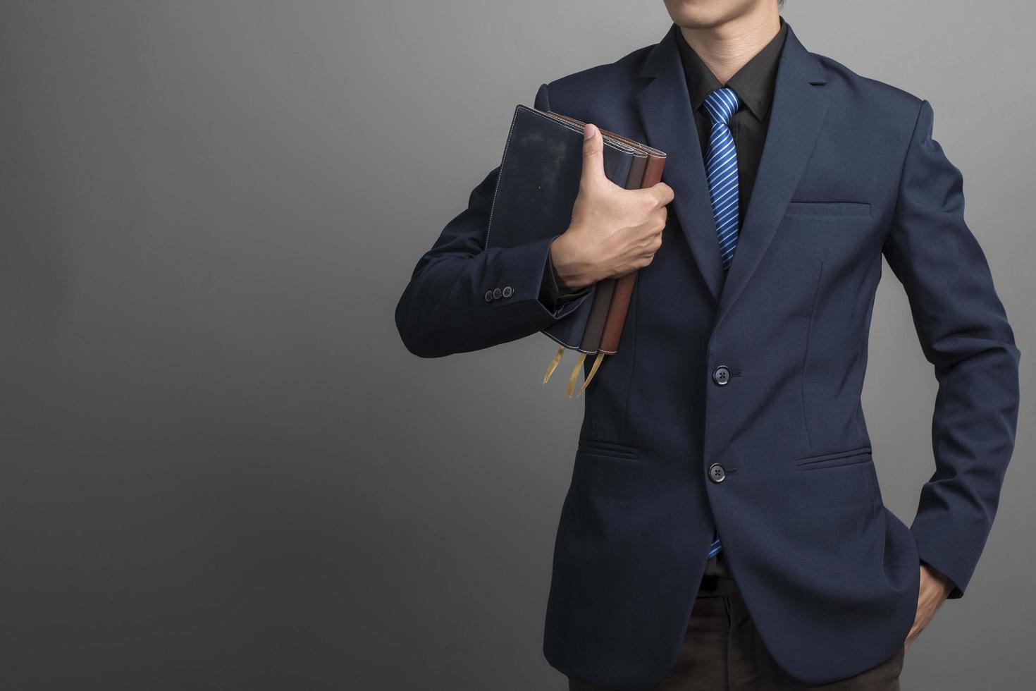 Cerca del empresario en traje azul sosteniendo libros sobre fondo gris foto