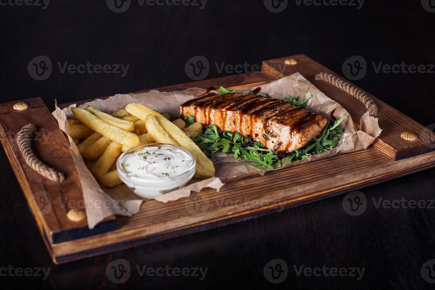 Filete de salmón con papas fritas en una bandeja de madera, hermosa porción, fondo oscuro foto