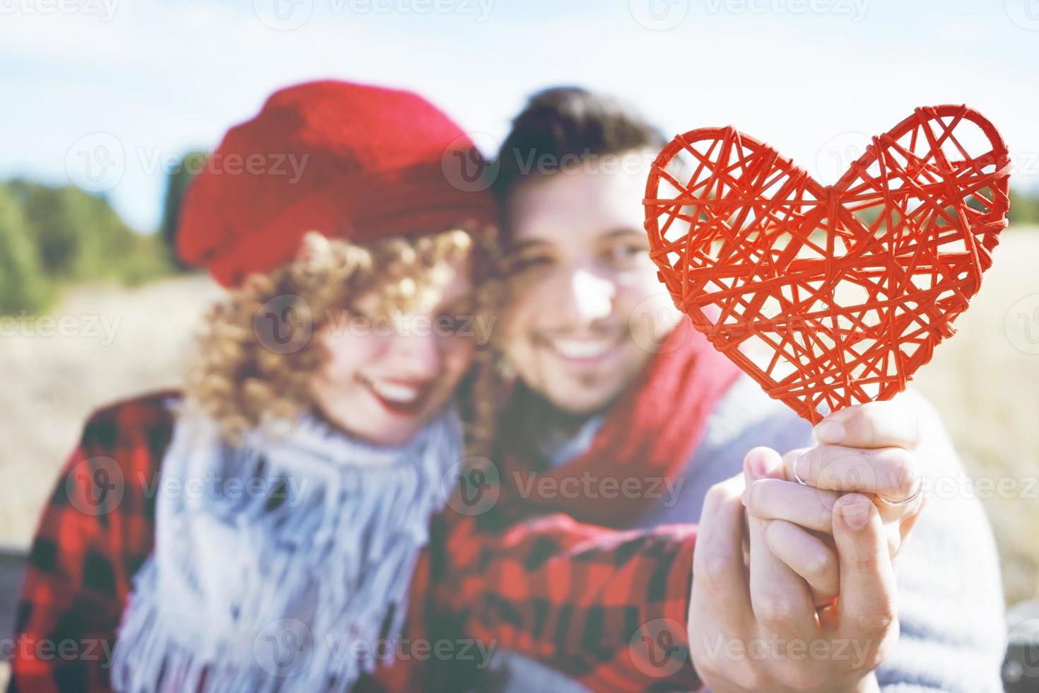 Lovely close-up of a beautiful red heart held by a romantic young couple in love in a nice bokeh as background outdoor. It reminds love or health care photo