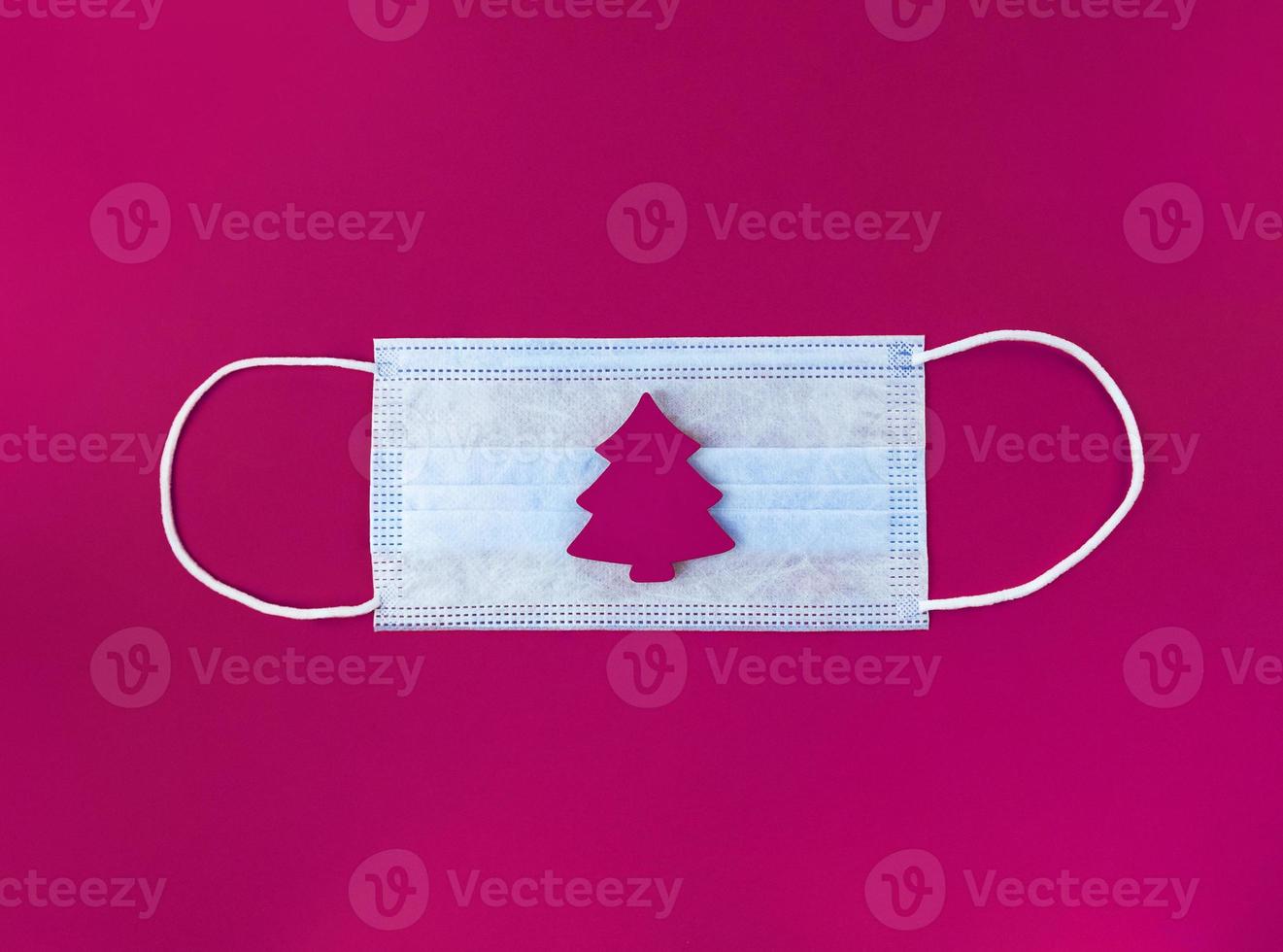 Medical mask and wooden christmas tree on a magenta background. photo