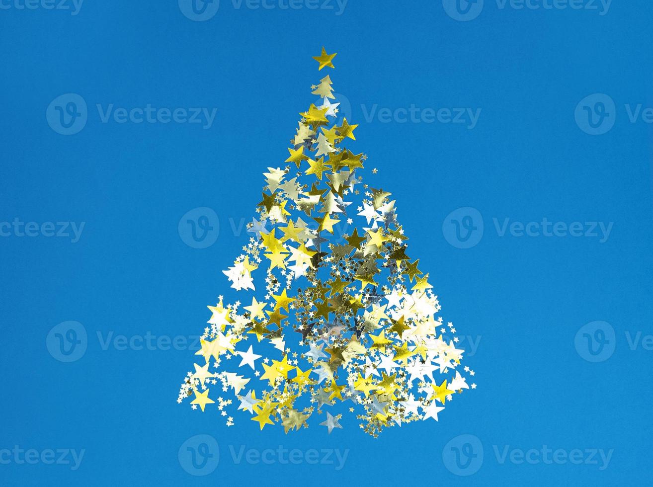 Christmas tree shape from golden confetti stars on a blue paper. photo