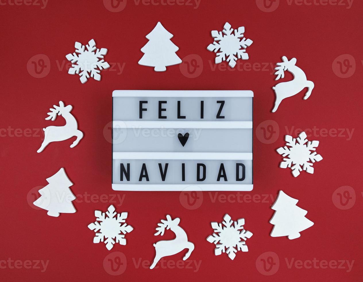 Light box with Feliz Navidad phrase, Spanish Merry Christmas on a red background with wooden toys. photo