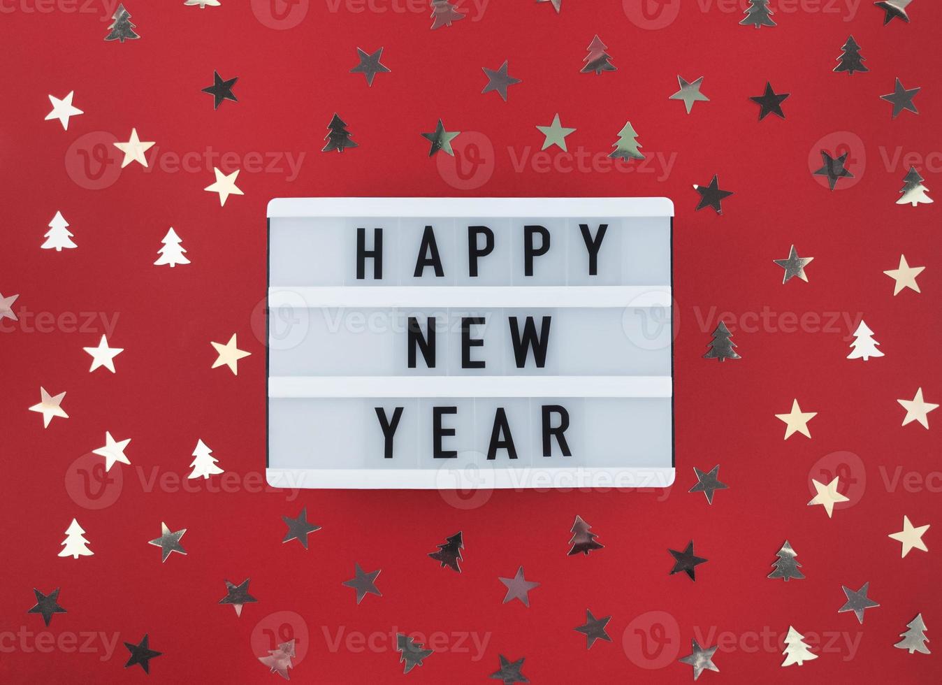 saludo de feliz año nuevo en caja de luz y confeti sobre un fondo rojo. foto