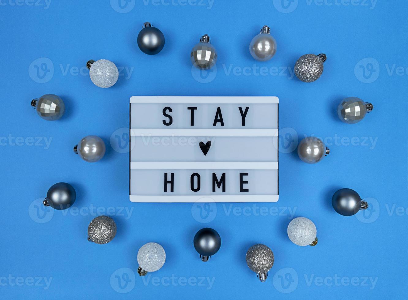Light box with stay home quote on a blue background with Christmas balls. photo