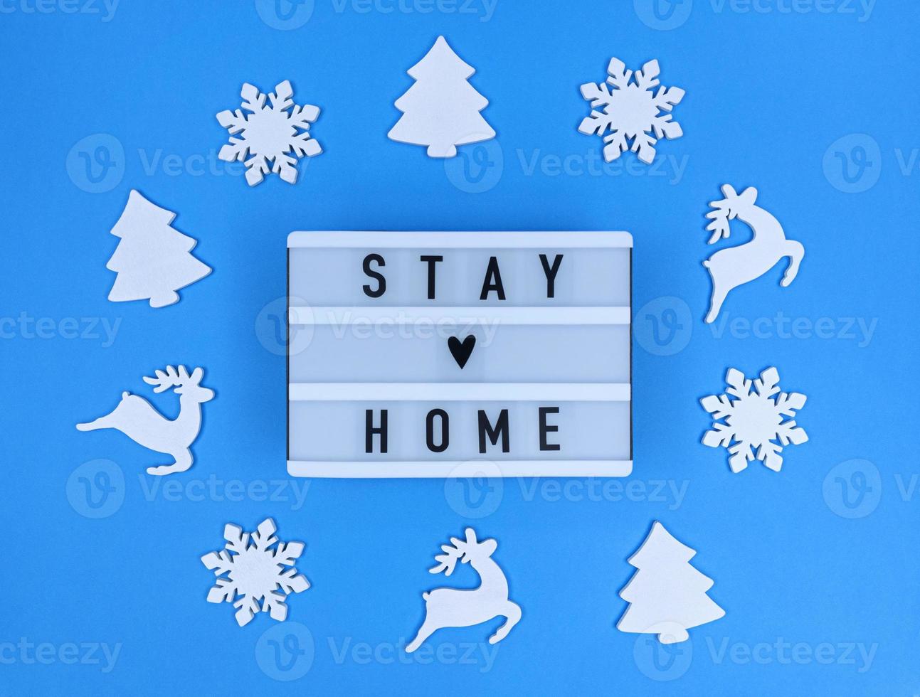 Light box with Stay home quote on a blue background with christmas toys. photo