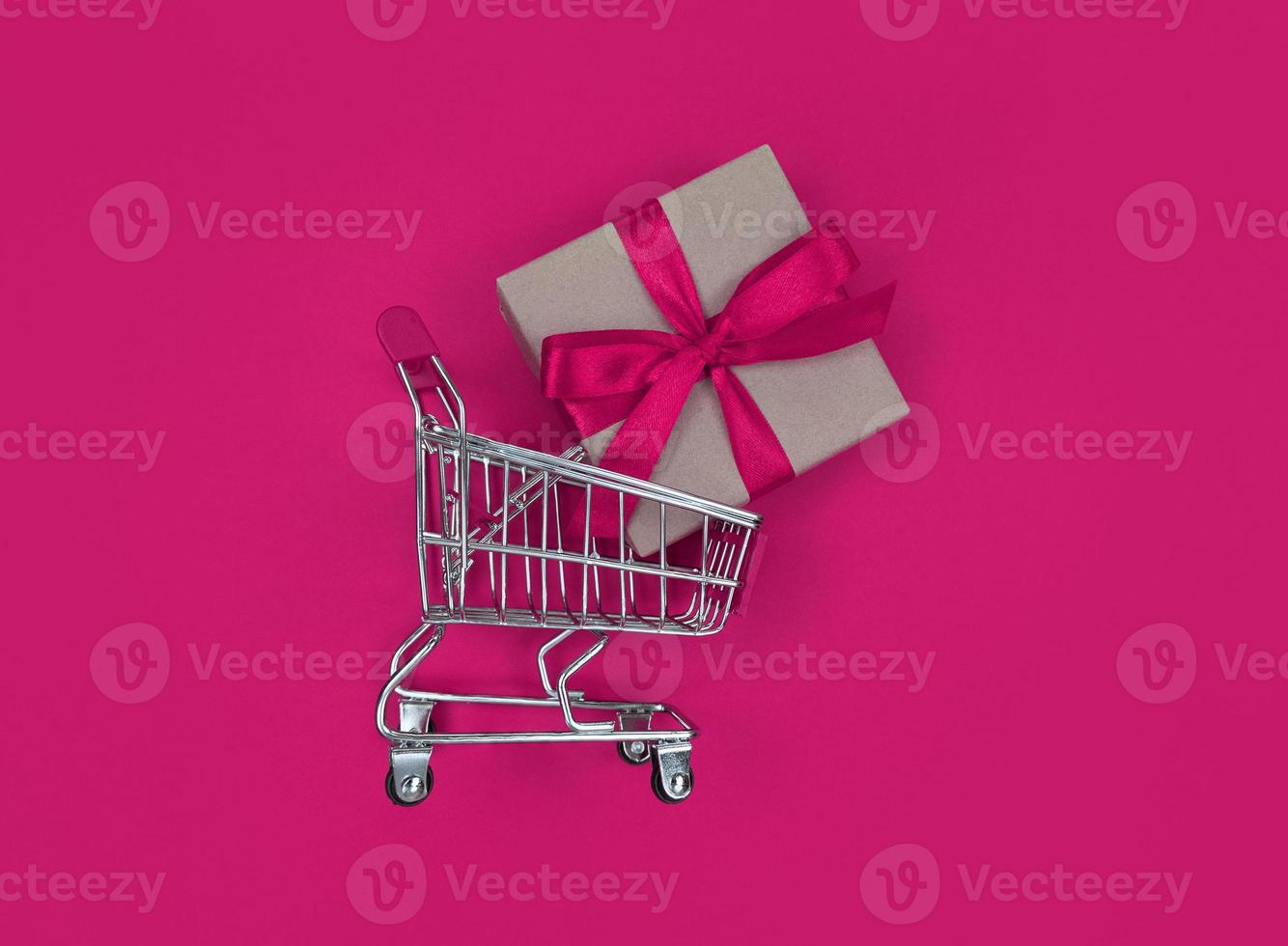 Supermarket trolley and gift box on pink background. Shopping concept. photo