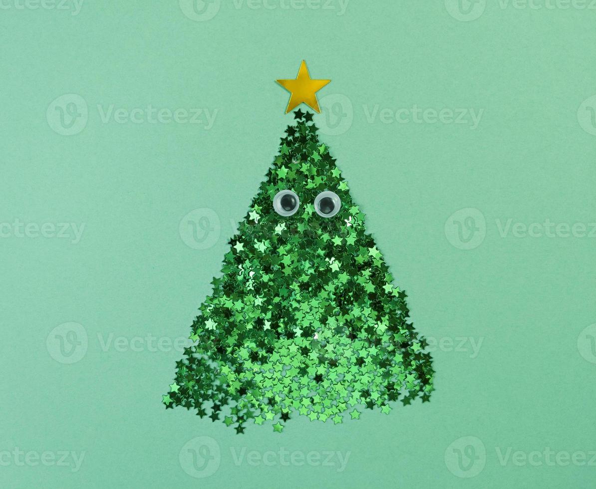Christmas tree shape from confetti stars with eyes on a green paper. photo
