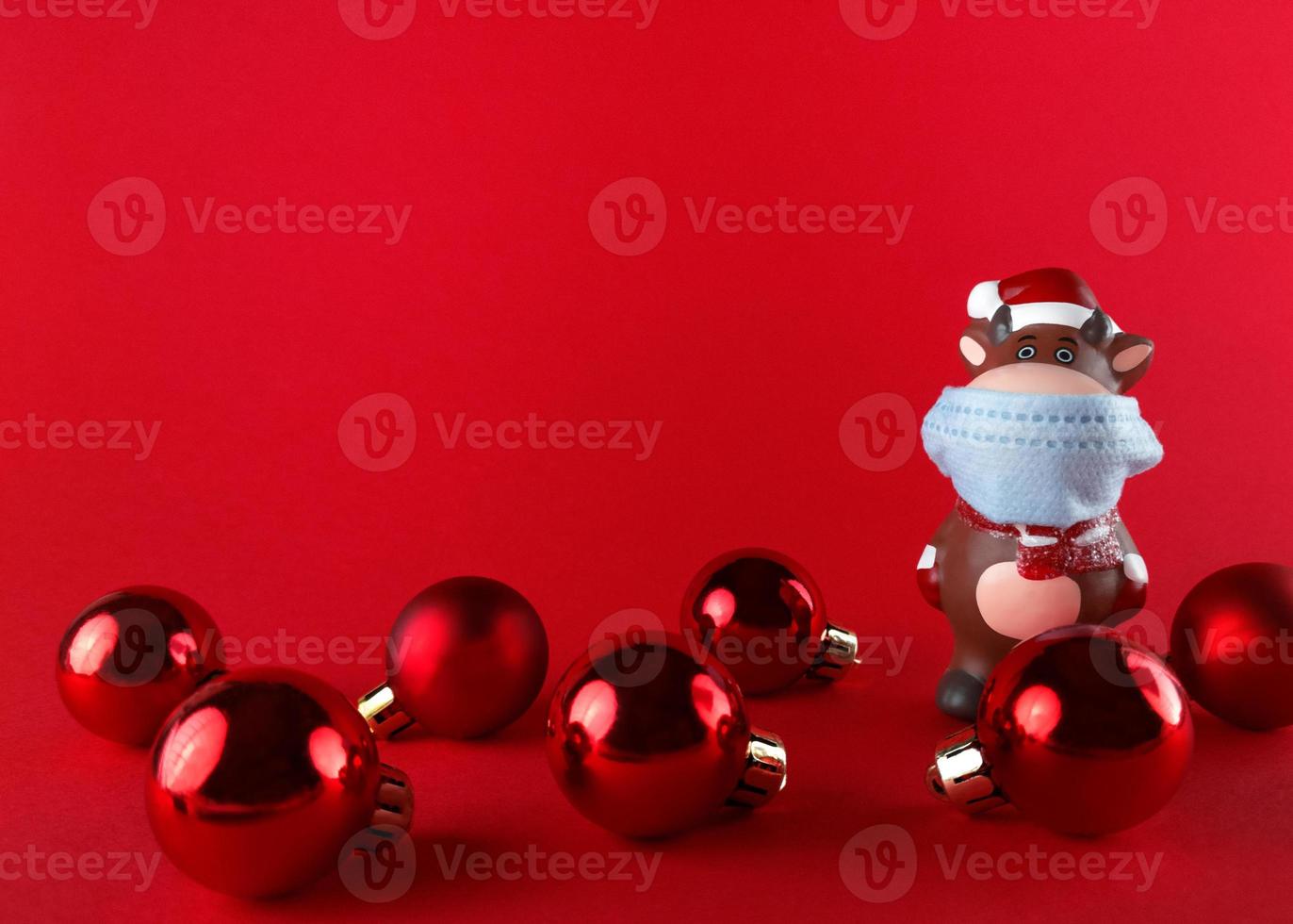 Ceramic statuette of Ox in medical mask and Christmas balls on red background with copy space. Symbol of new year 2021. photo