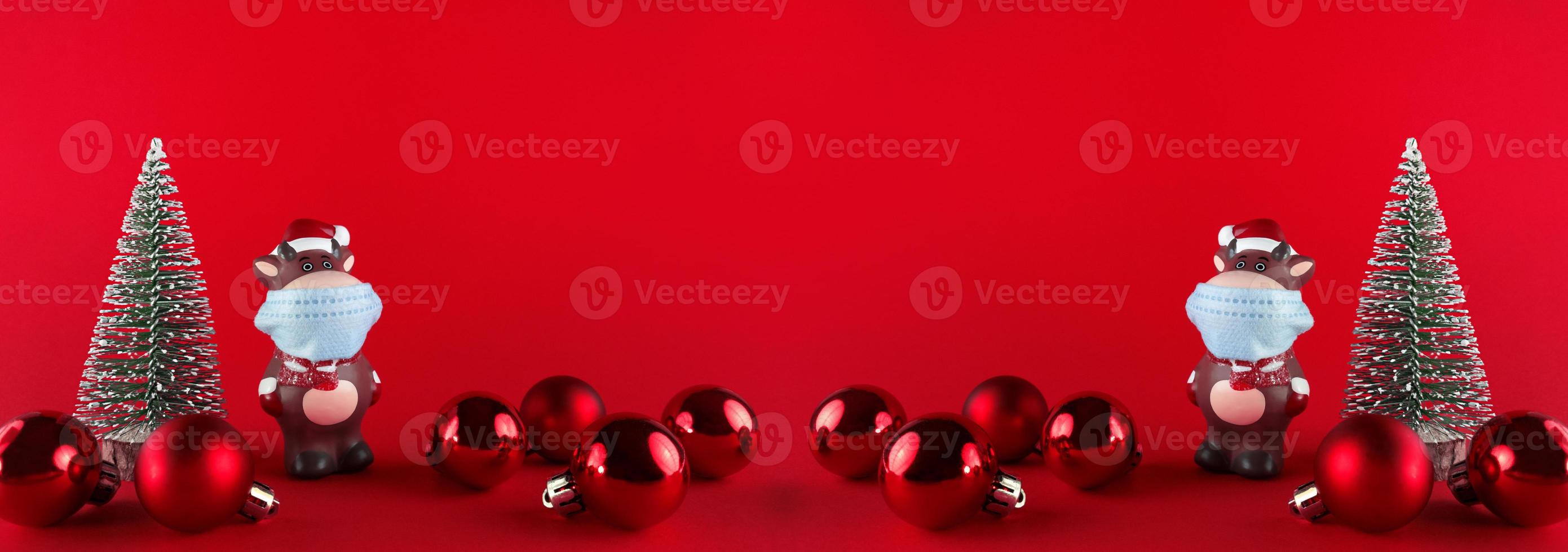 Ceramic statuettes of Ox in medical mask, Christmas trees and balls on red backgroud. Wide banner with copy space. Symbol of New Year 2021. photo