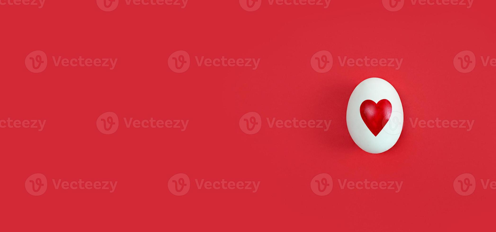 White egg with heart shape on red background with copy space. photo
