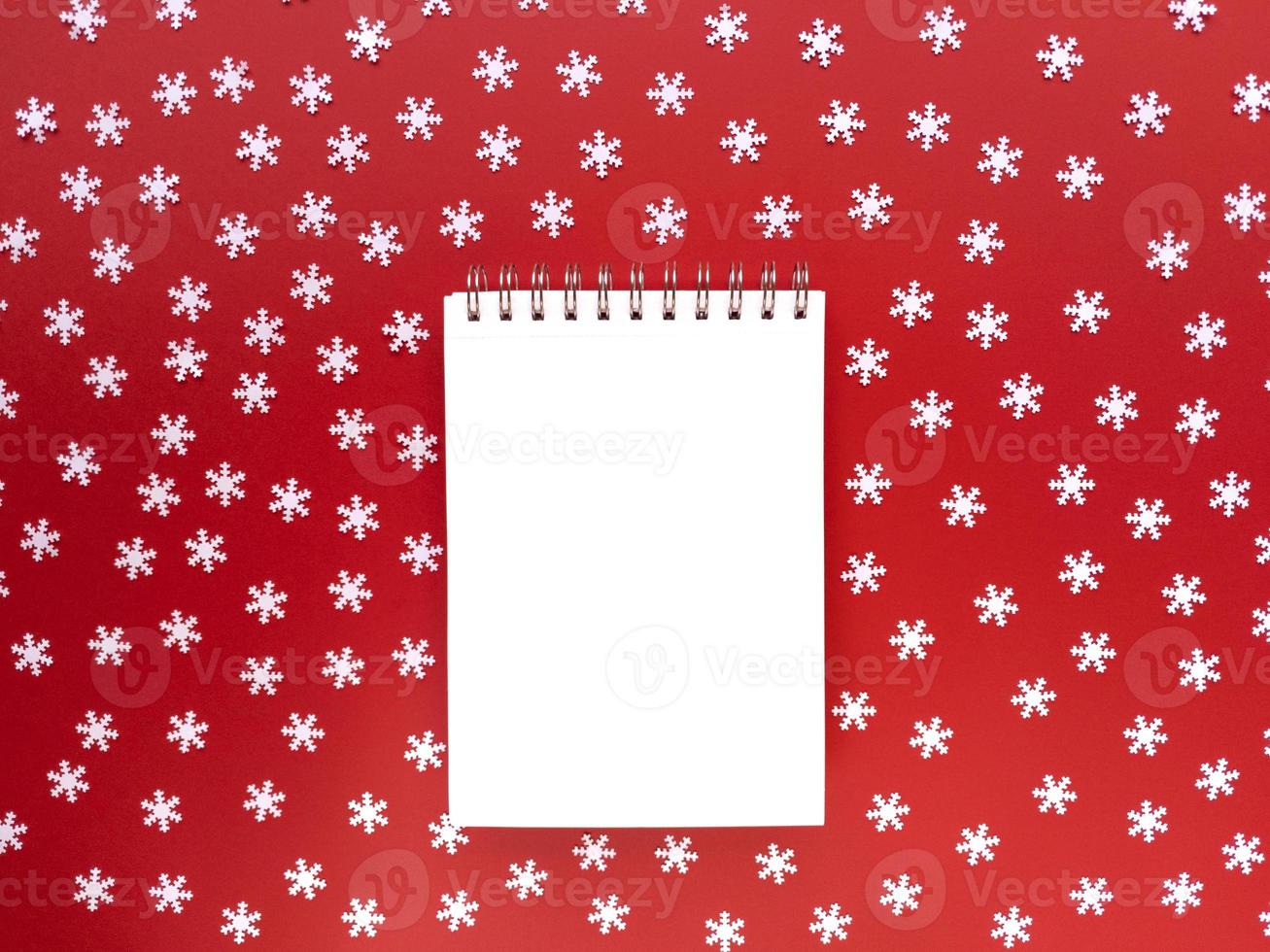 Blank sheet of notebook with scattered white snowflakes on red background. Educational concept. Simple flat lay with copy space. Stock photo. photo