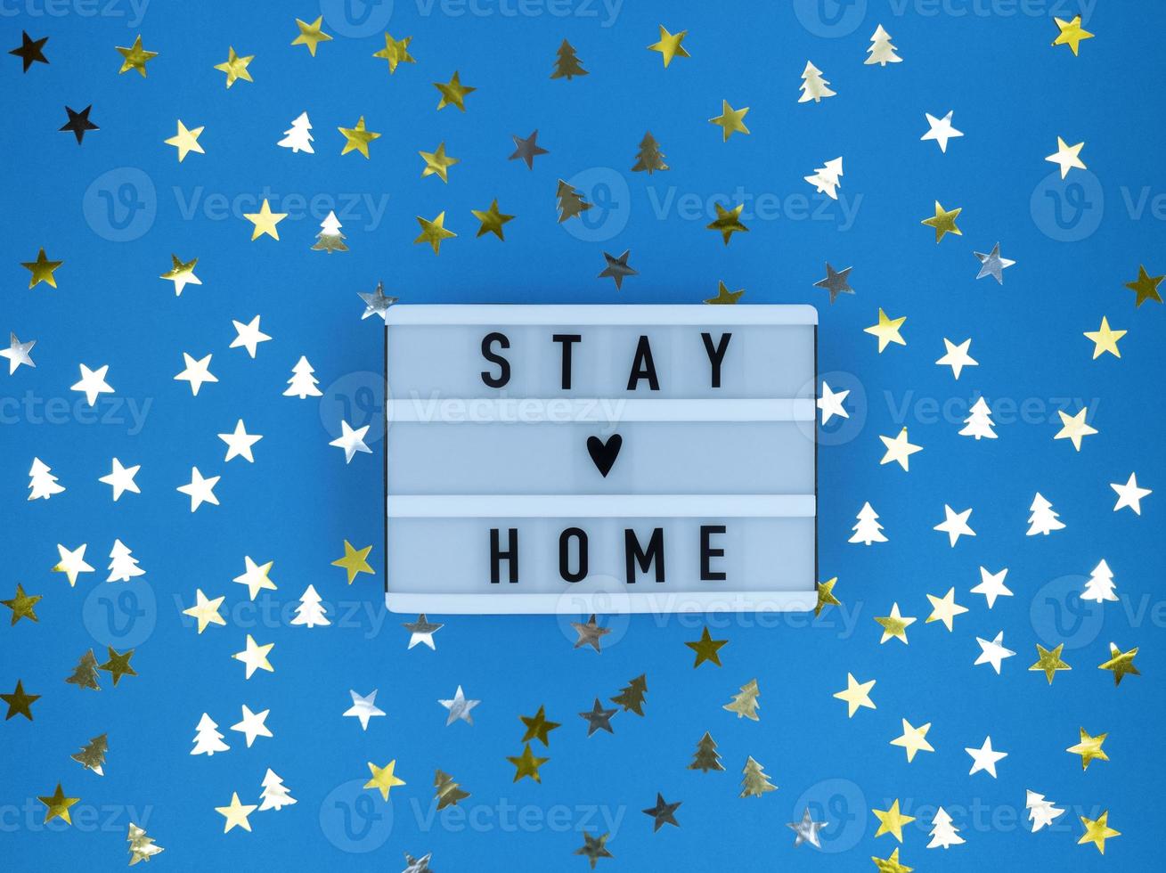 Light box with Stay home quote on a blue background with confetti. Christmas quarantine. photo