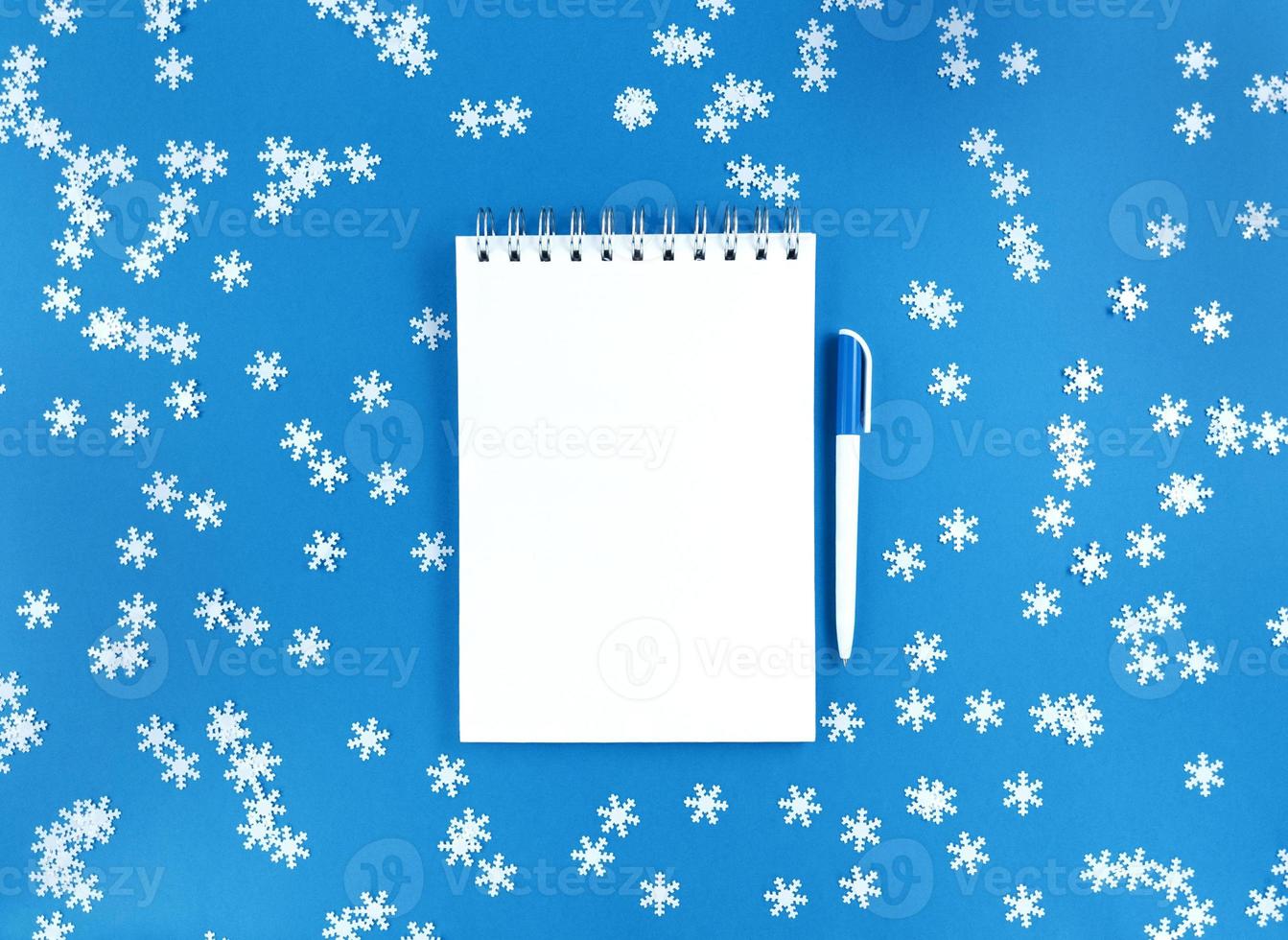 hoja de cuaderno en blanco blanco y un bolígrafo sobre un fondo azul con copos de nieve de confeti dispersos. concepto de educación de vacaciones. foto de stock.
