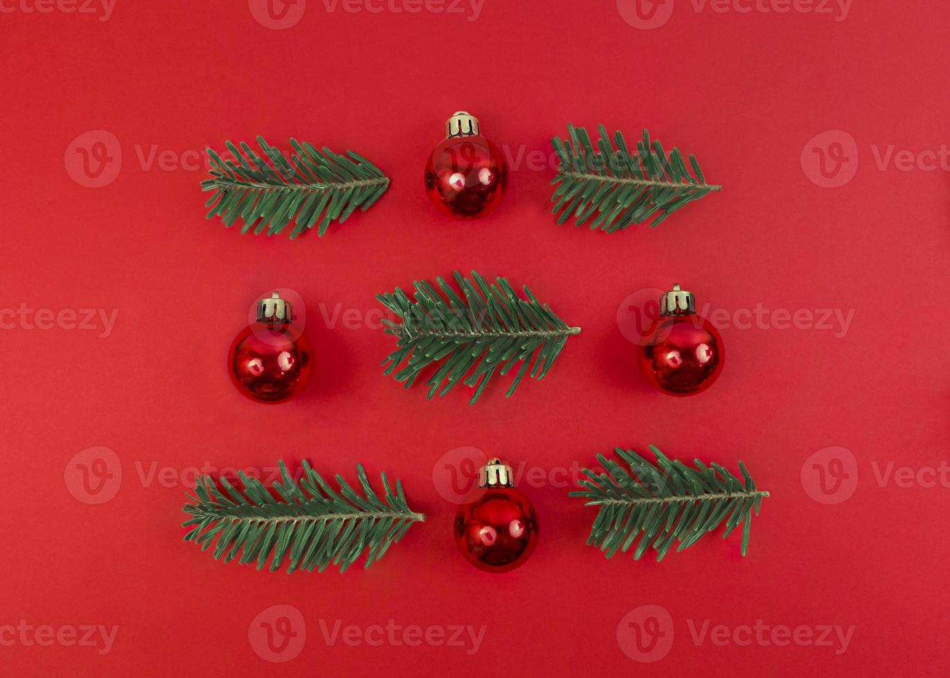 Composición de simetría navideña de adornos de juguete y ramas de abeto sobre un fondo rojo. plano festivo simple. foto