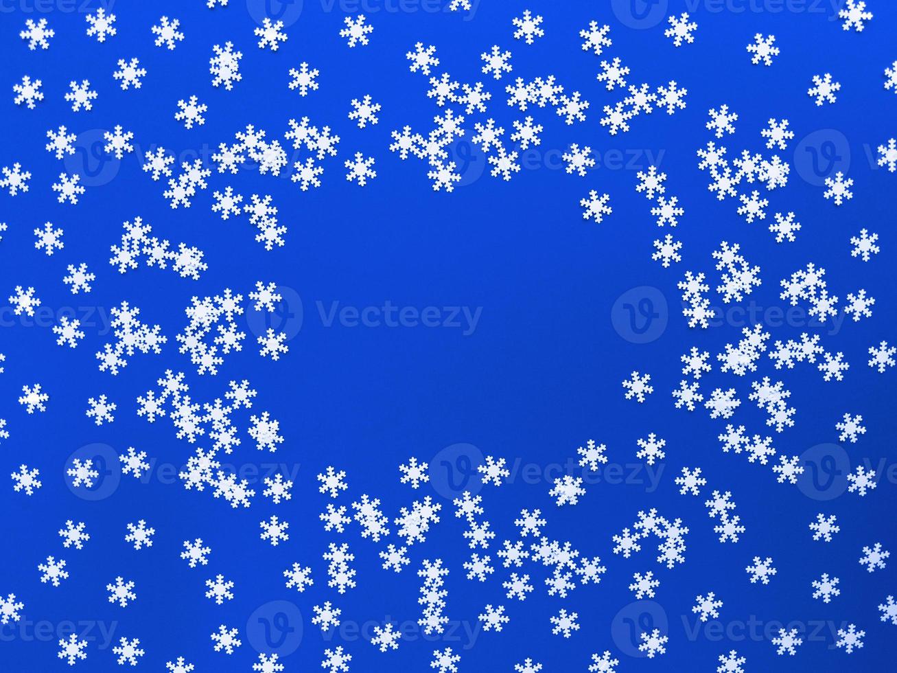 Scattered white snowflakes on blue background. Simple flat lay with copy space. Stock photo. photo