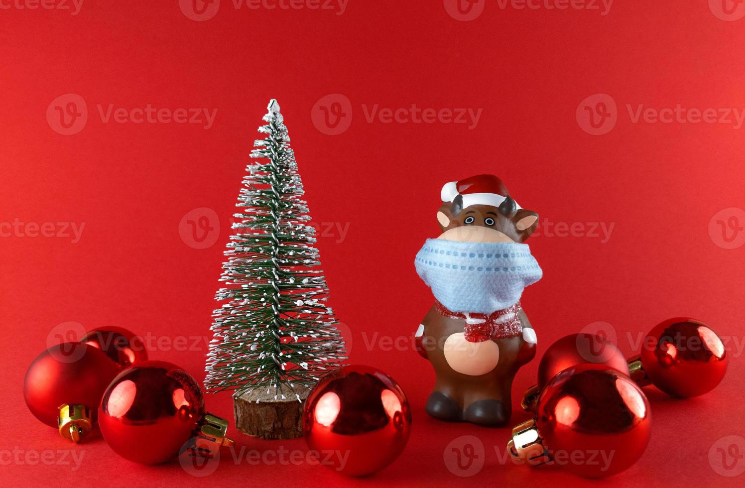 Ceramic statuette of Ox in medical mask, Christmas tree and balls on a red backgroud. Symbol of New Year 2021. photo