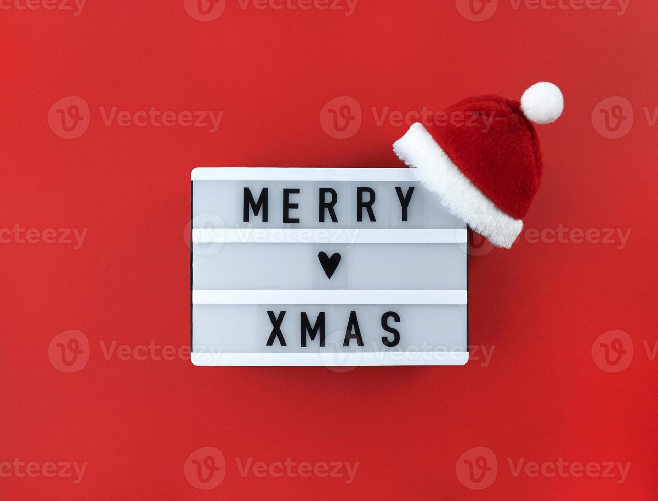 Merry xmas greeting on light box with Santa hat on a red background. photo