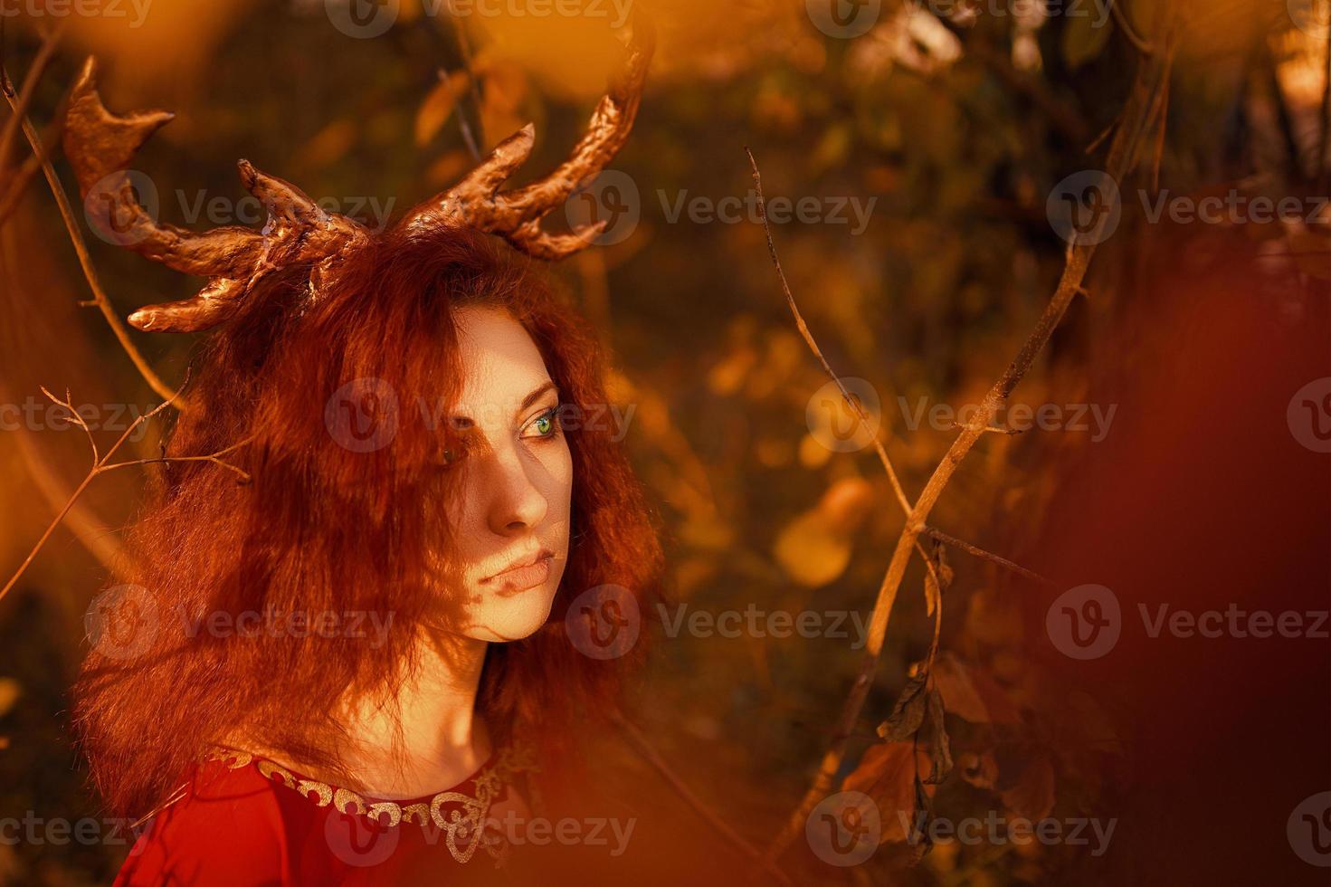 Woman in long red dress with deer horns in autumn forest. photo
