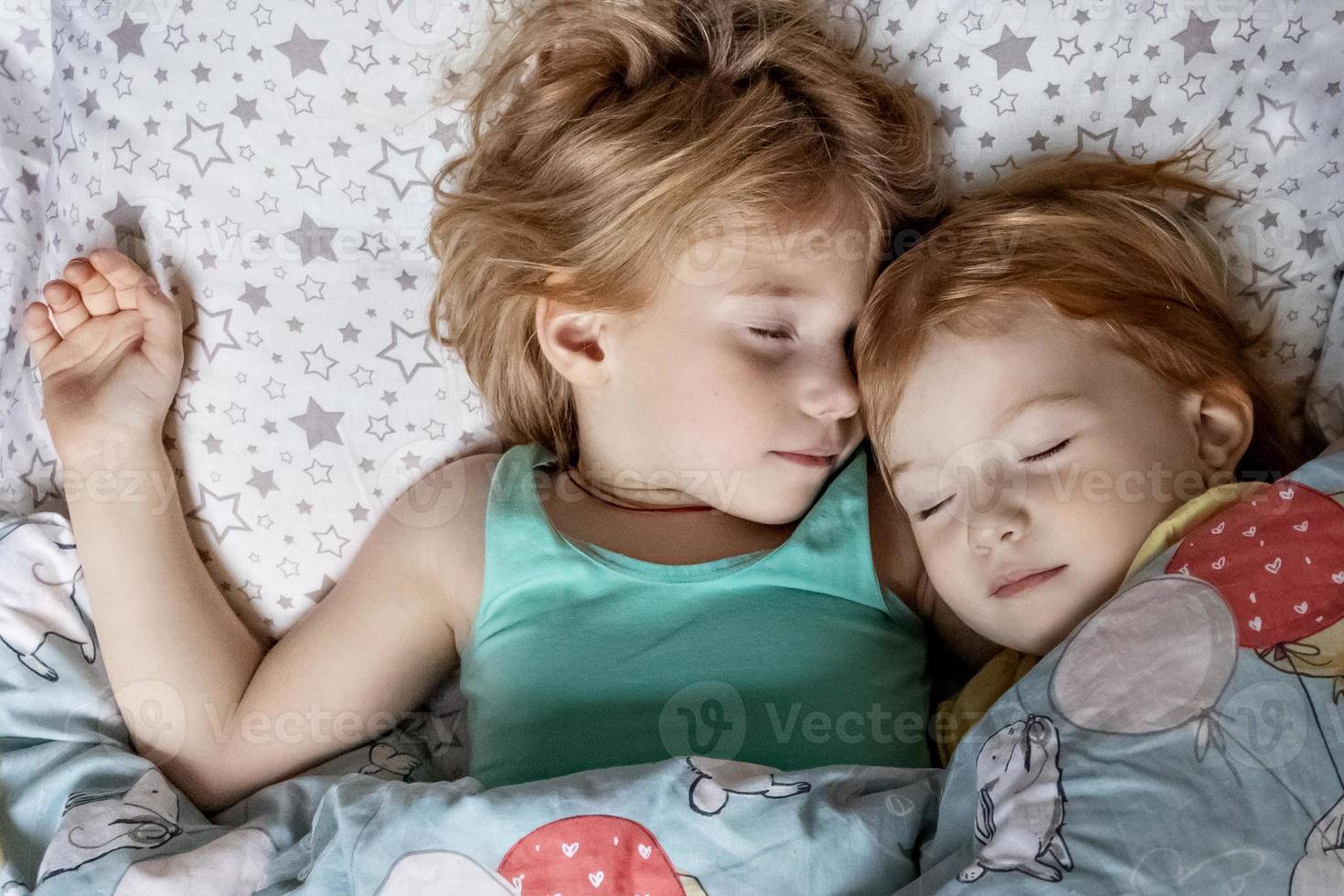 Dos hermanitas hermanas durmiendo en un abrazo en la cama debajo de una manta foto