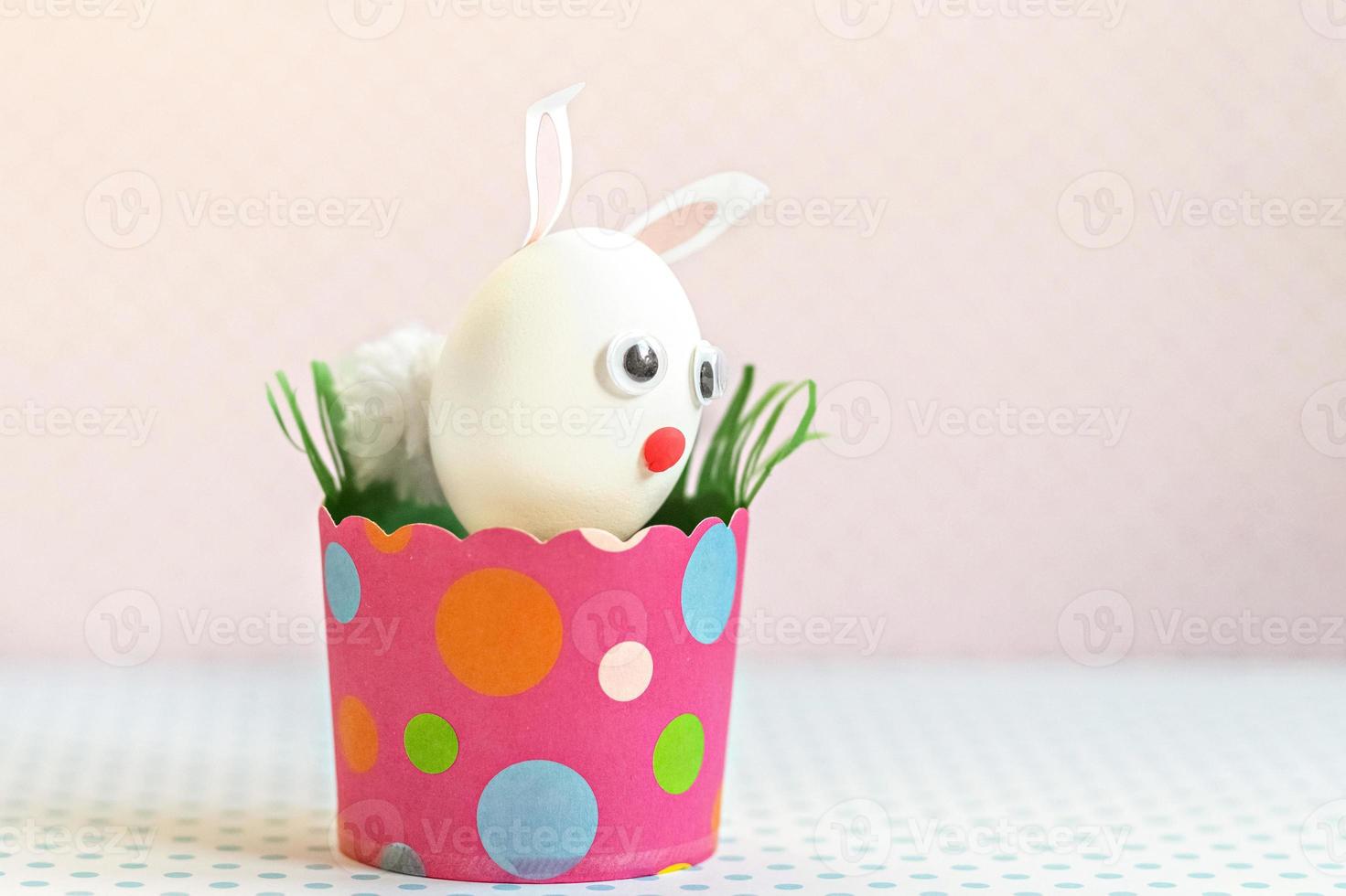 huevo de gallina blanco con orejas de conejo y bozal en una bandeja de papel rosa ecológico, caja. feliz concepto de vacaciones de pascua. foto