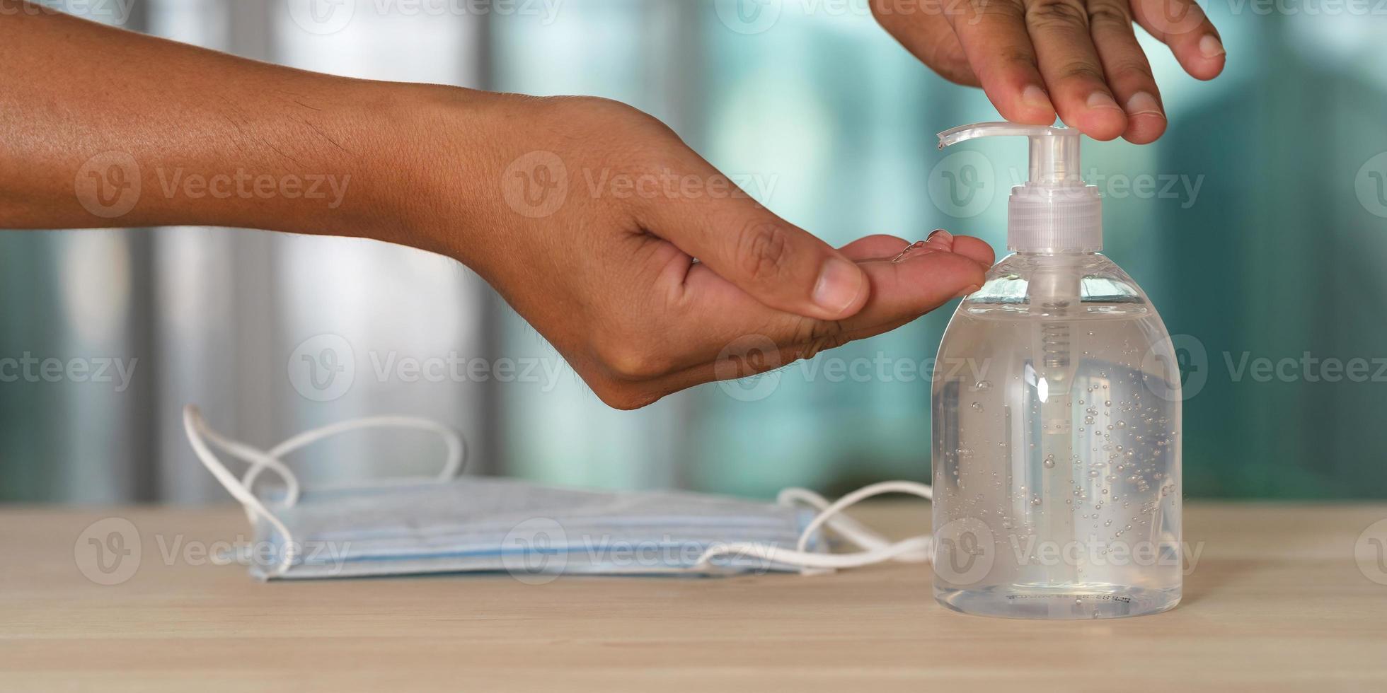 Mano con gel de alcohol desinfectante de manos y mascarilla médica en la mesa foto