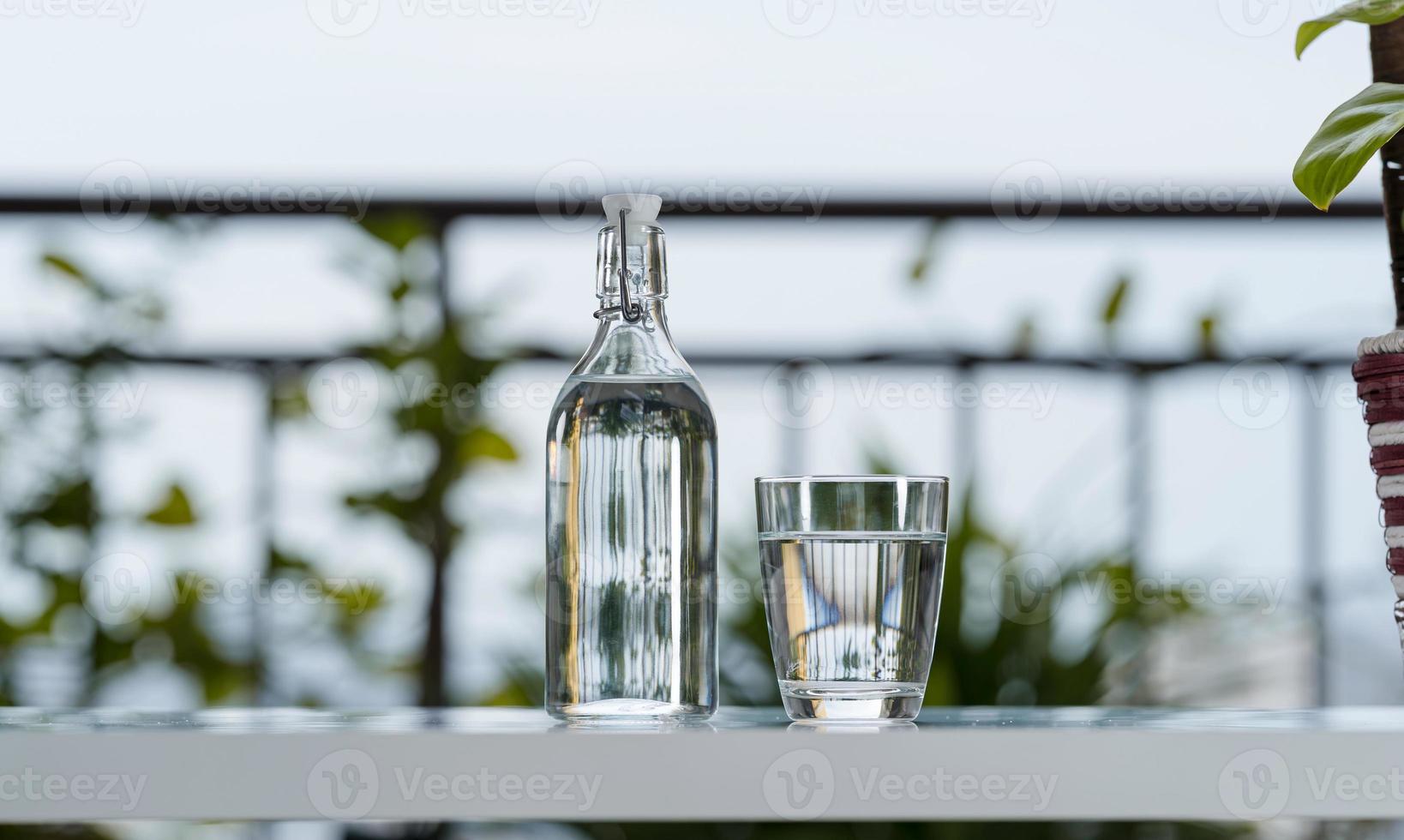 Beber una botella de agua con vidrio sobre la mesa en el jardín de la casa foto