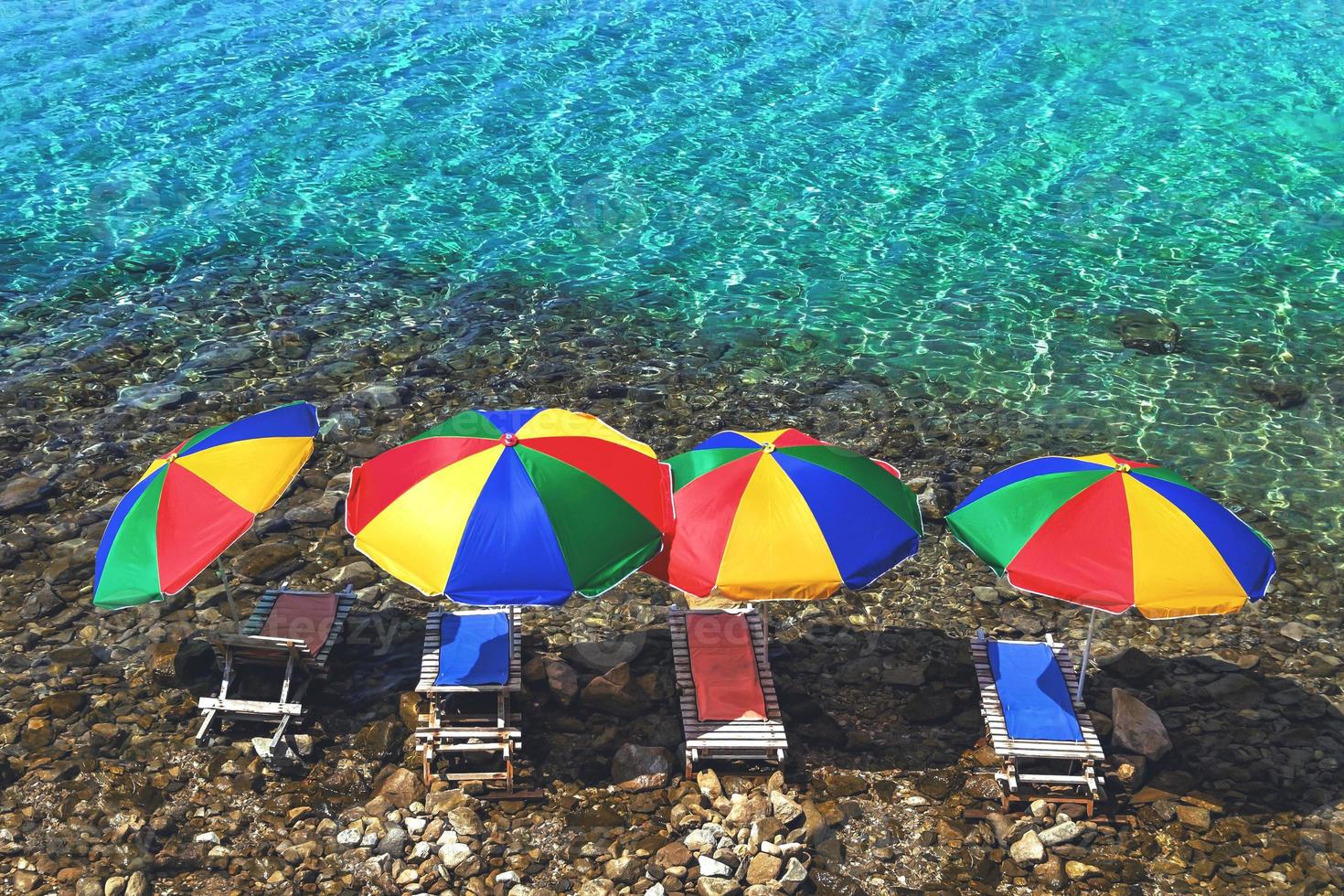 Four beach umbrellas and sunbeds in the water on the stone beach photo