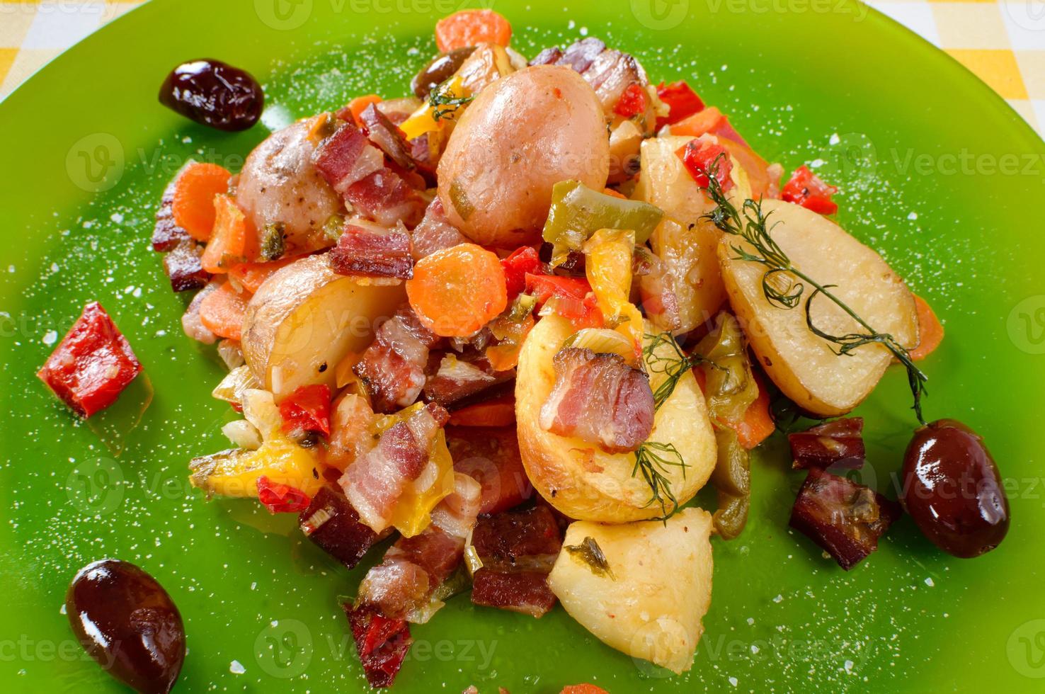 Potatoes baked with bacon, paprika, carrots, onions and several spices, herbs and olives served on plate. photo