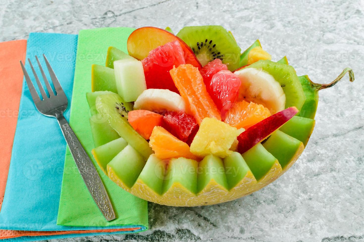 Ensalada de frutas frescas con kiwi, plátano, melocotón, naranja, naranja roja, albaricoque y melón en un tazón de piña artesanal. foto