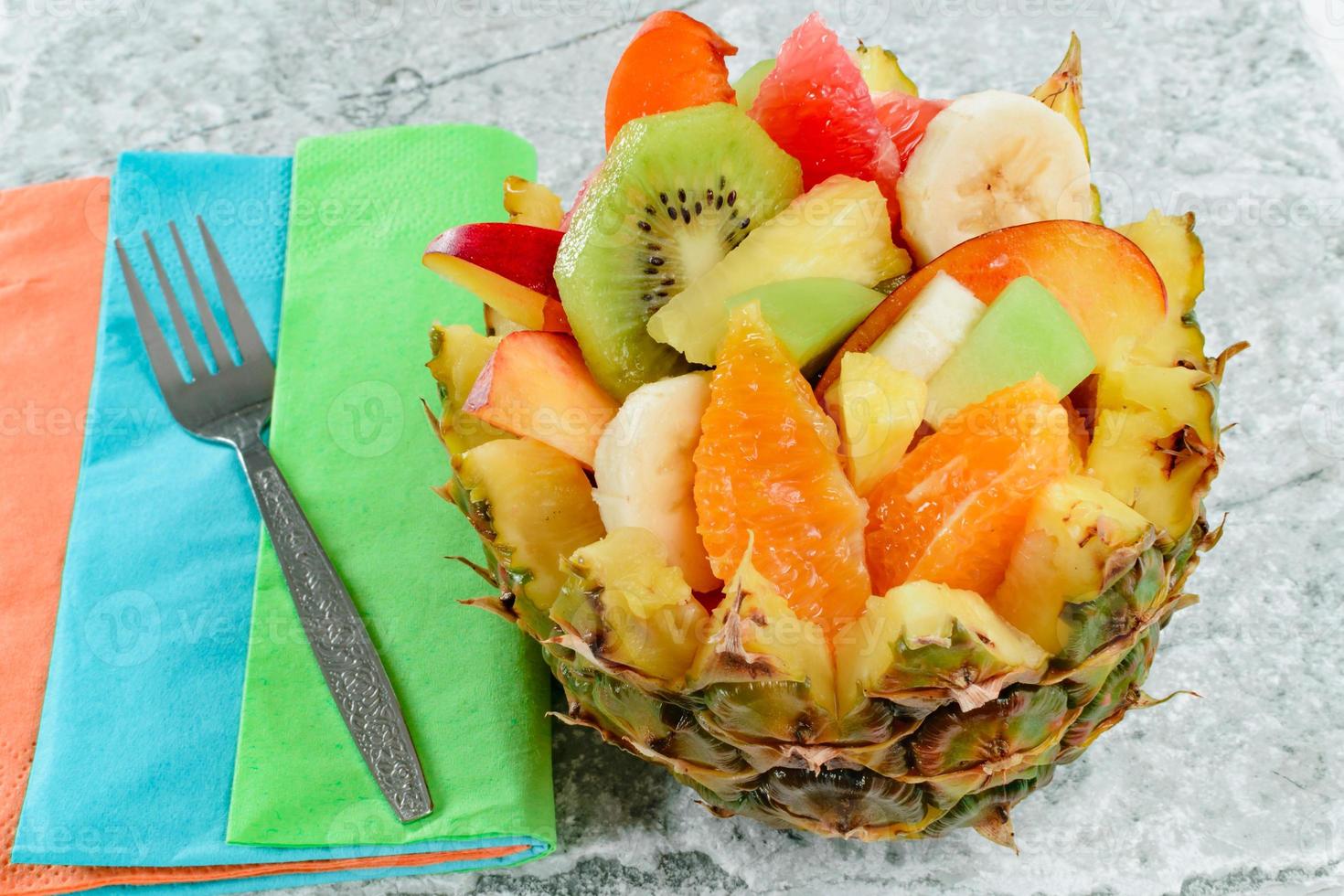 Ensalada de frutas frescas con kiwi, plátano, melocotón, naranja, naranja roja, albaricoque y melón en un tazón de piña artesanal. foto