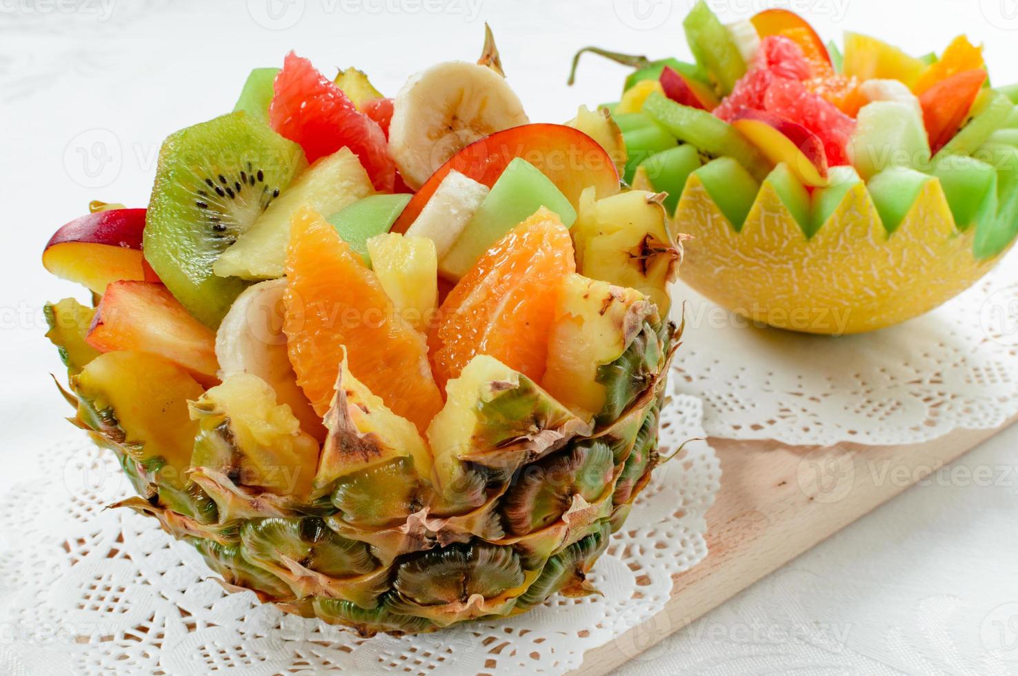 Ensalada de dos frutas frescas con kiwi, plátano, melocotón, naranja, naranja roja, albaricoque y melón en un tazón artesanal de melón y piña. foto