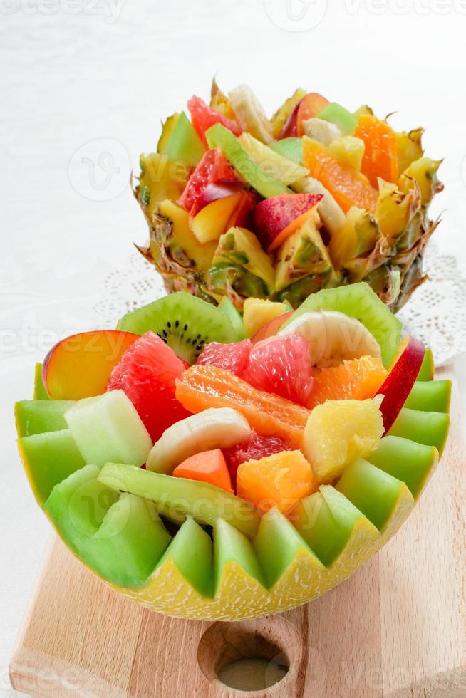 Ensalada de dos frutas frescas con kiwi, plátano, melocotón, naranja, naranja roja, albaricoque y melón en un tazón artesanal de melón y piña. foto