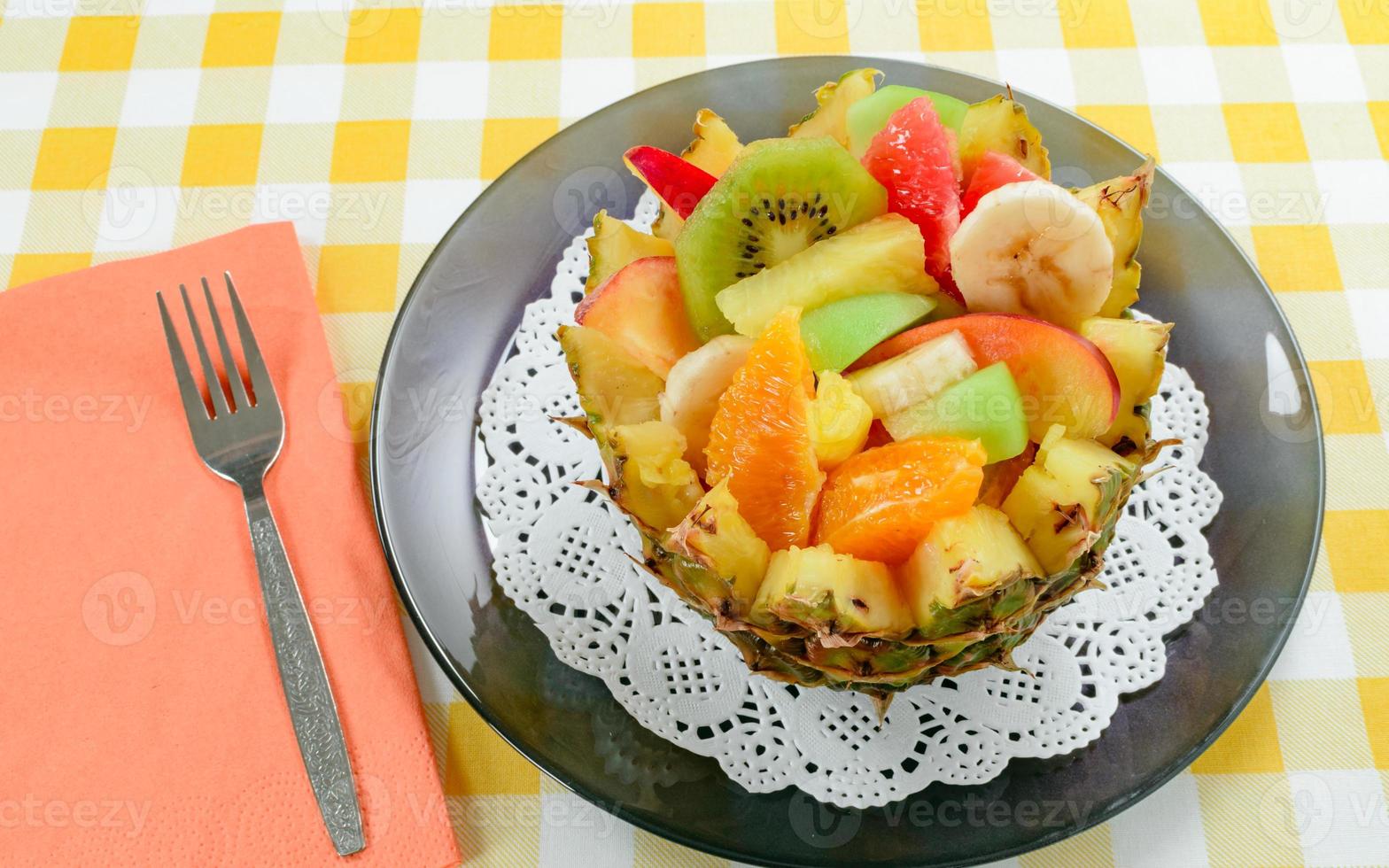 Ensalada de frutas frescas con kiwi, plátano, melocotón, naranja, naranja roja, albaricoque y melón en un tazón de piña artesanal. foto