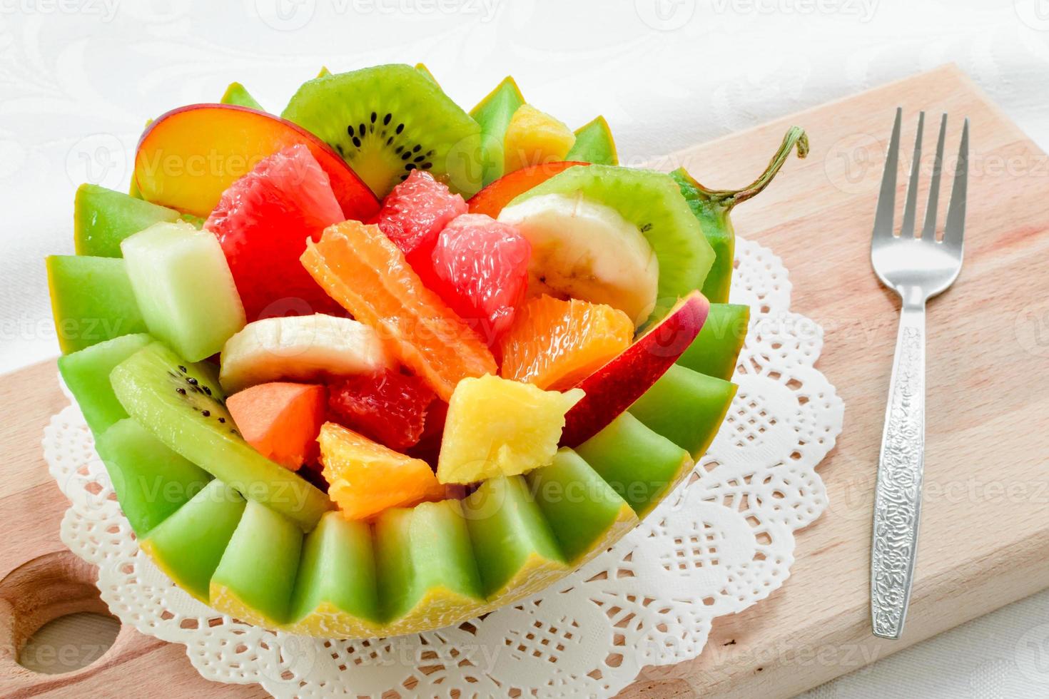 Ensalada de frutas frescas con kiwi, plátano, melocotón, naranja, naranja roja, albaricoque y melón en un tazón de piña artesanal. foto