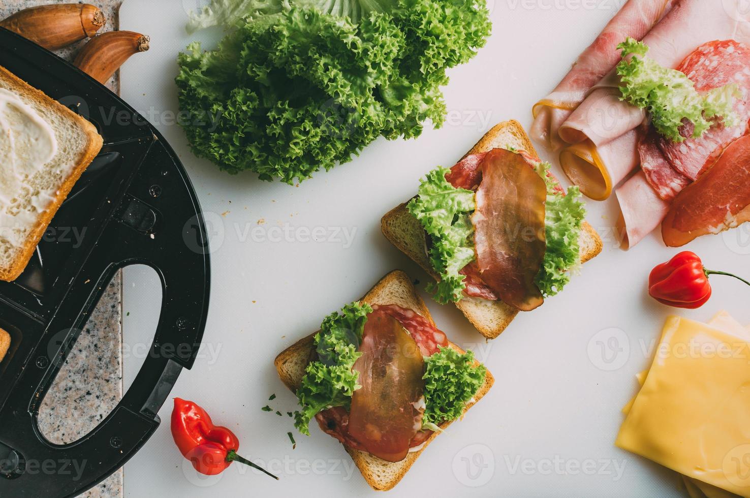 Club sandwich with ham, salami, smoked beef, cheese, lettuce and arugula. Toast sandwich preparation. Top view. photo