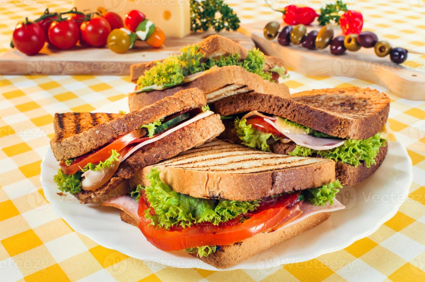 sándwich club con jamón, salami, ternera ahumada, queso, lechuga y rúcula.Preparación de sándwich tostado. foto