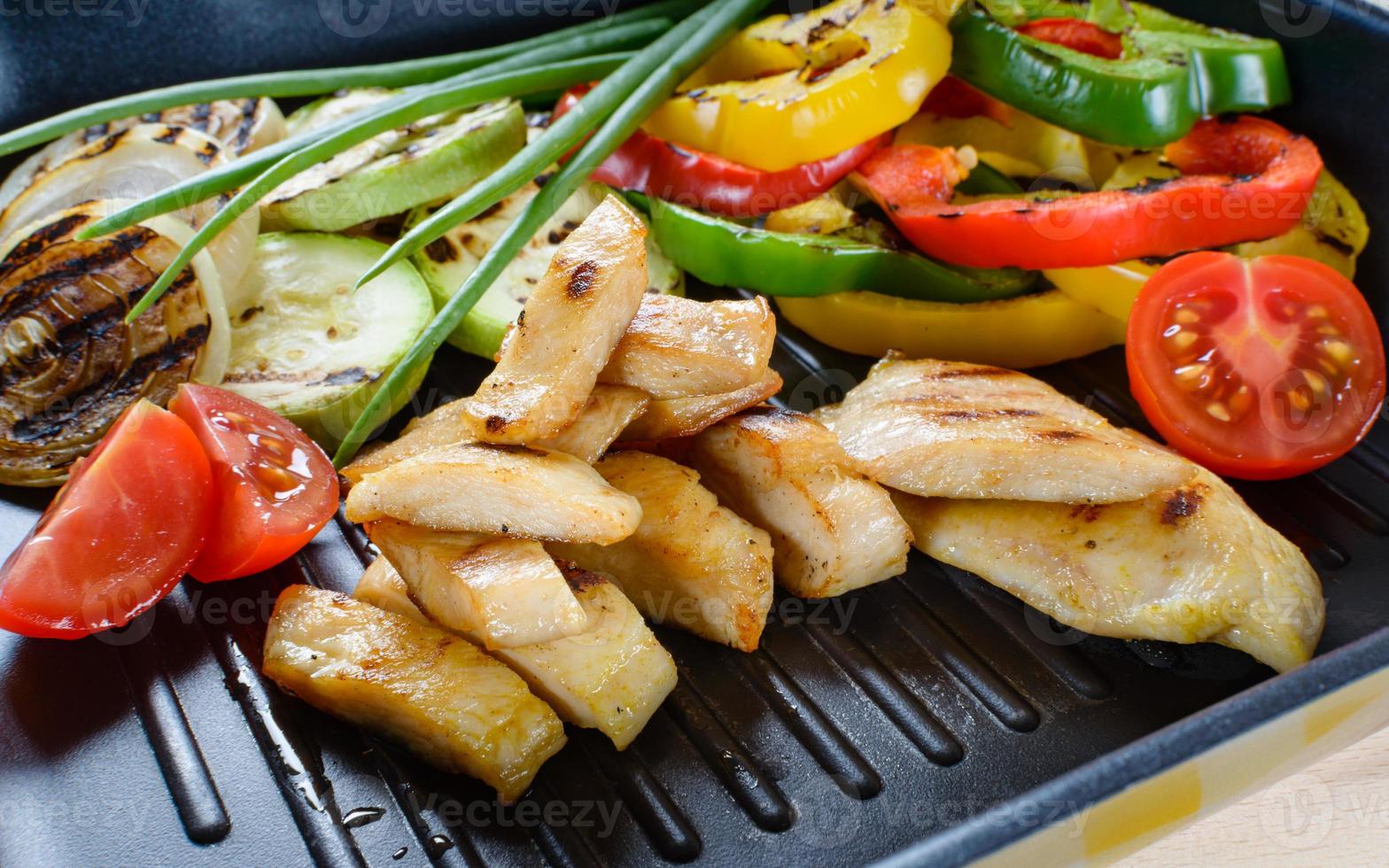 Grilled chicken meat on grill with vegetables in the background. photo