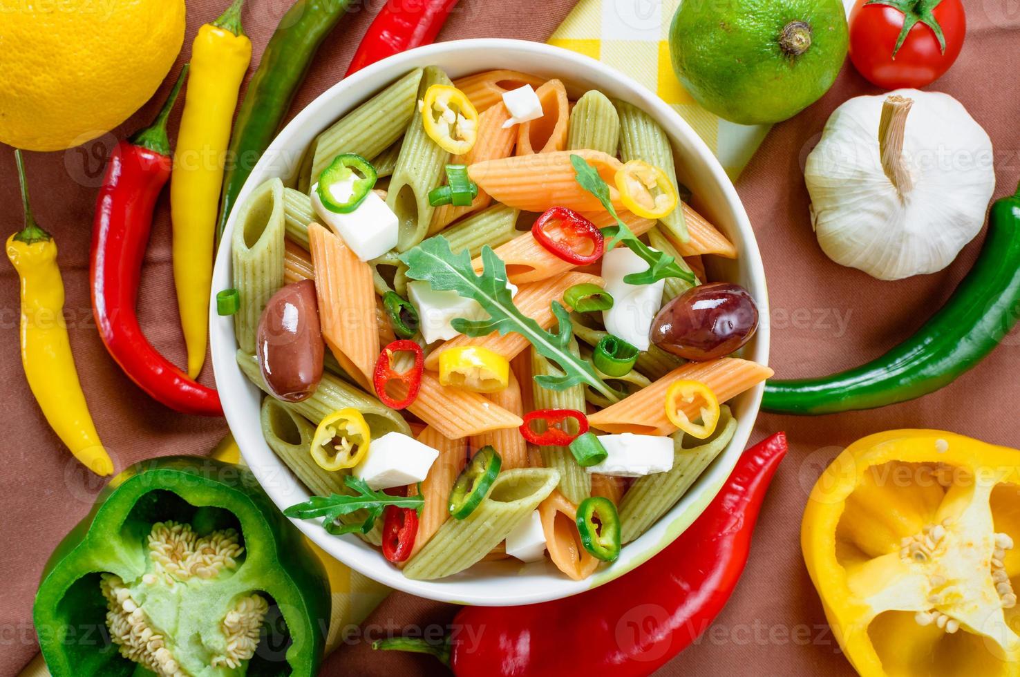 Pasta salad with tomato,arugula, cucumber, peppers,hot peppers, black and green olives, and cheese feta. Top view. photo