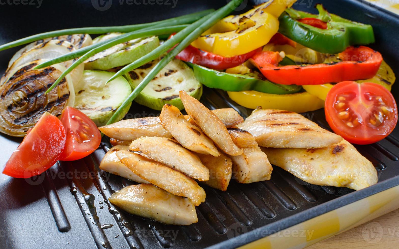 Grilled chicken meat on grill with vegetables in the background. photo