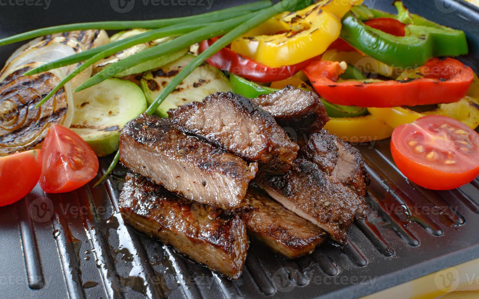 Grilled beef meat on grill with grilled vegetables in the background. photo